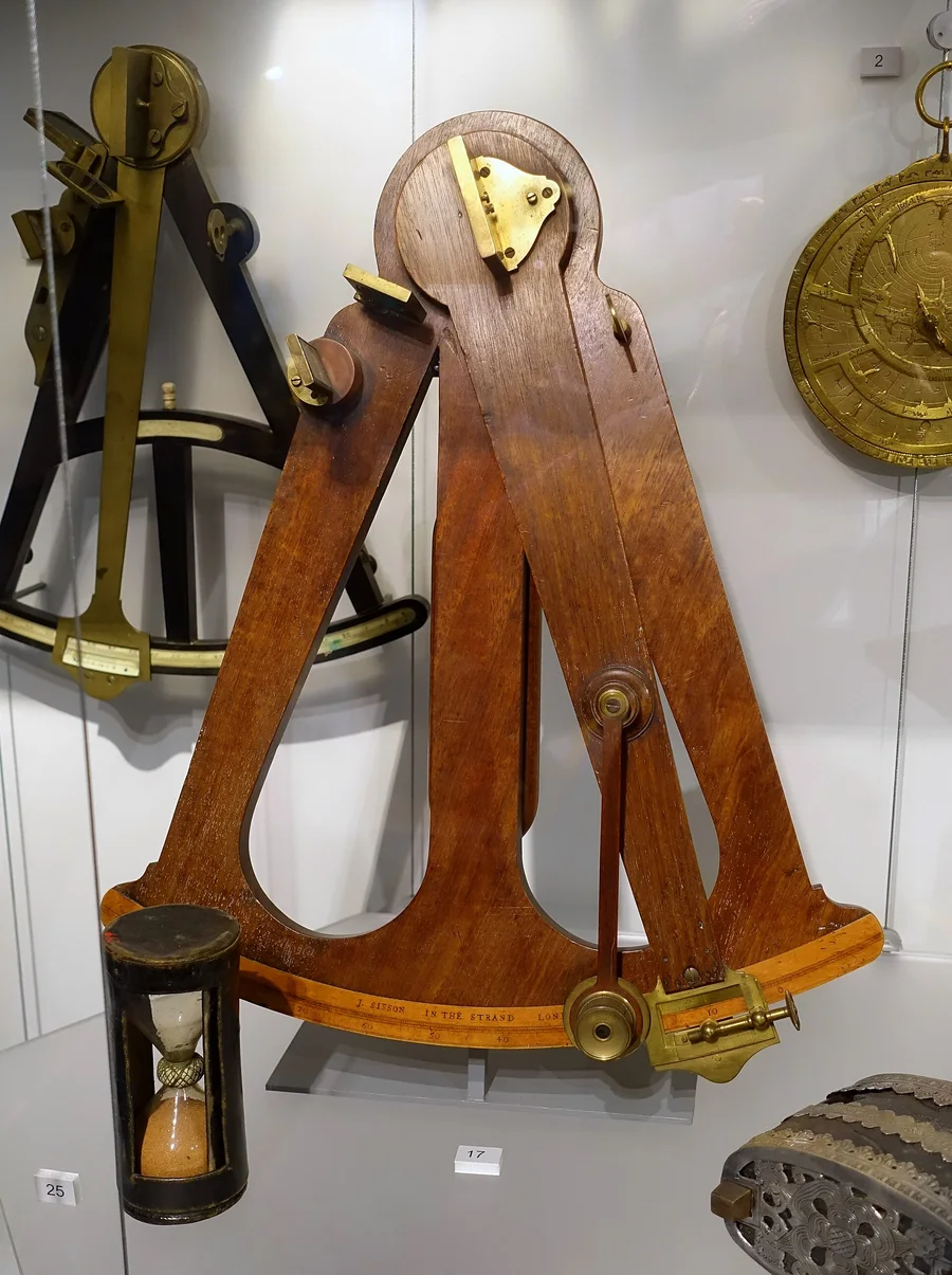 A wooden Hadley octant with its two mirrors and brass index arm, with an hourglass in front.